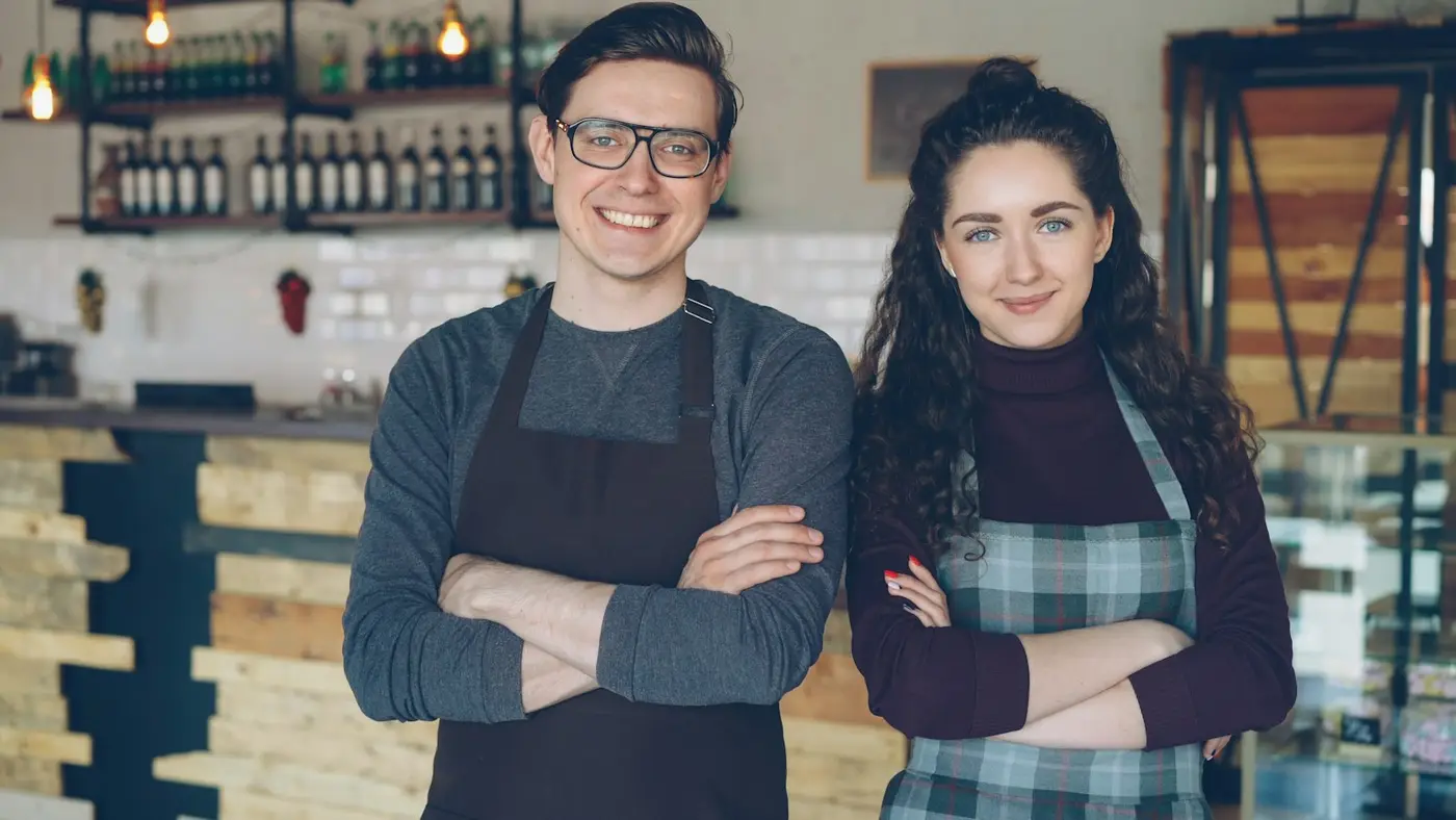 Casal dono de um café, de avental, no balcão do próprio negócio